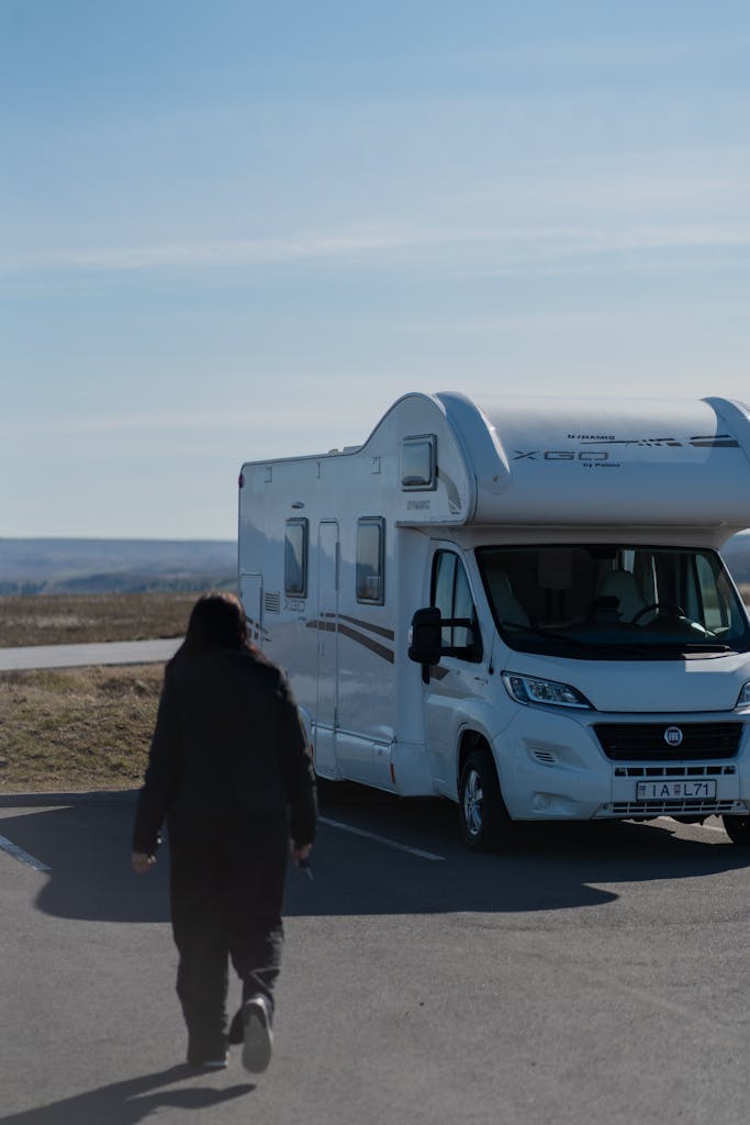 A person approaches a parked camper van in a sunny, rural landscape, capturing a sense of adventure.