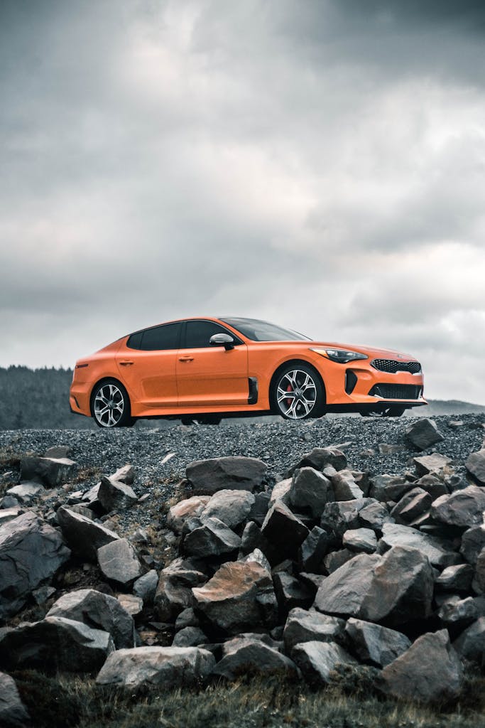 Orange car parked on rocky terrain under a cloudy sky, perfect for automotive themes.